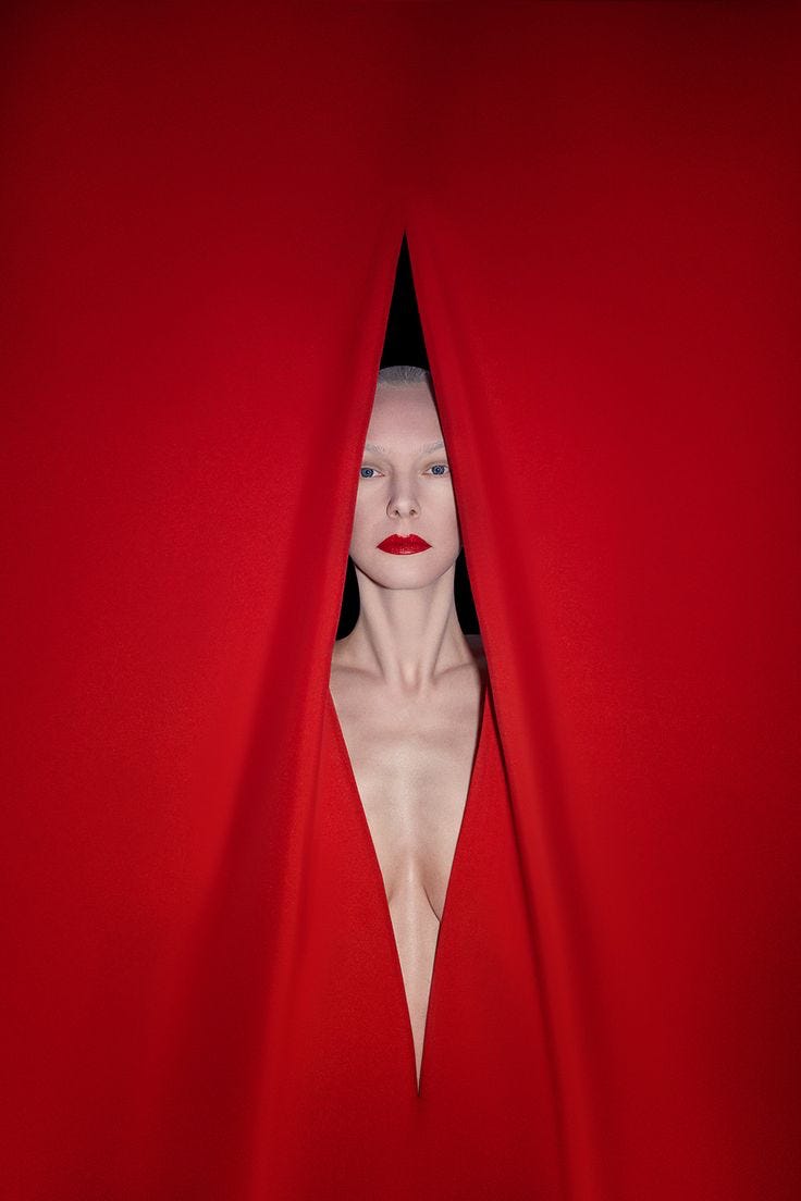 High-fashion portrait of a woman with red lipstick emerging from dramatic red fabric curtains, avant-garde editorial photography.