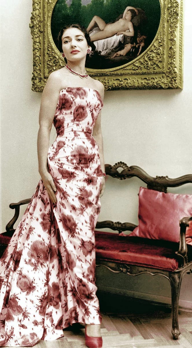 A woman stands in front of a painting wearing a strapless white dress embellished with a painterly red print.