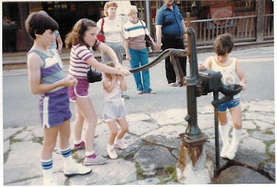 My 3 siblings and I at an old water pump. I'm working the pump with a big camera case hanging around my neck. My 3 siblings and I at an old water pump. I'm working the pump with a big camera case hanging around my neck.