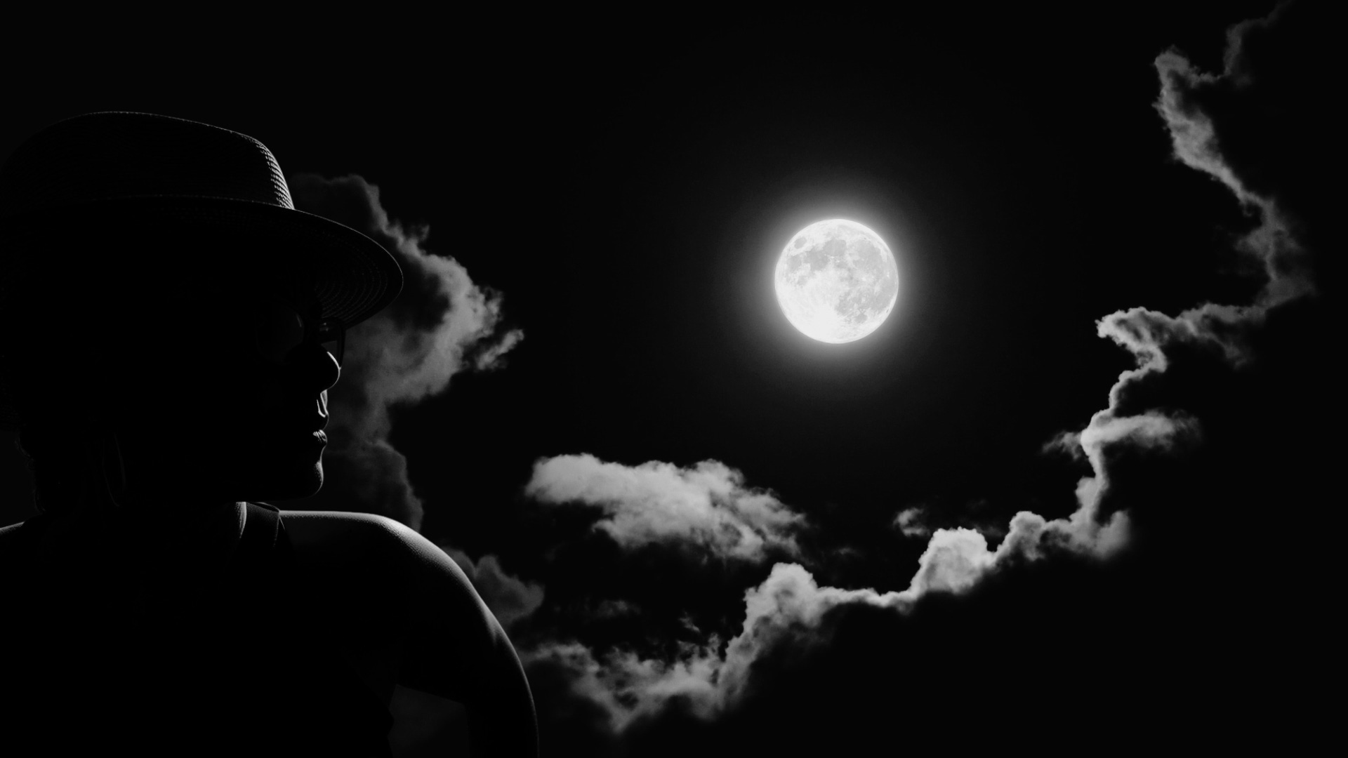 Imagen de Cibelle con sombrero y de perfil sobre un fondo de cielo nublado y luna llena en blanco y negro y alto contraste.