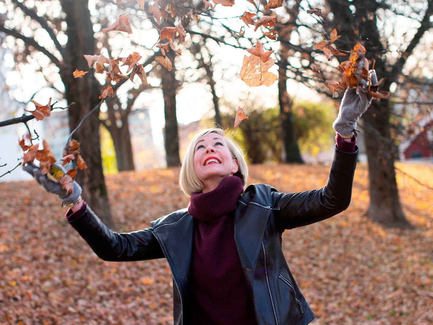 Image of Hannah, tossing a handful of fall leaves over hear head, smiling
