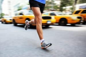 Running in New York City - man city runner jogging in street of Manhattan with yellow taxi caps cars and traffic. Urban lifestyle image of male jogger training downtown. Legs and running shoes.