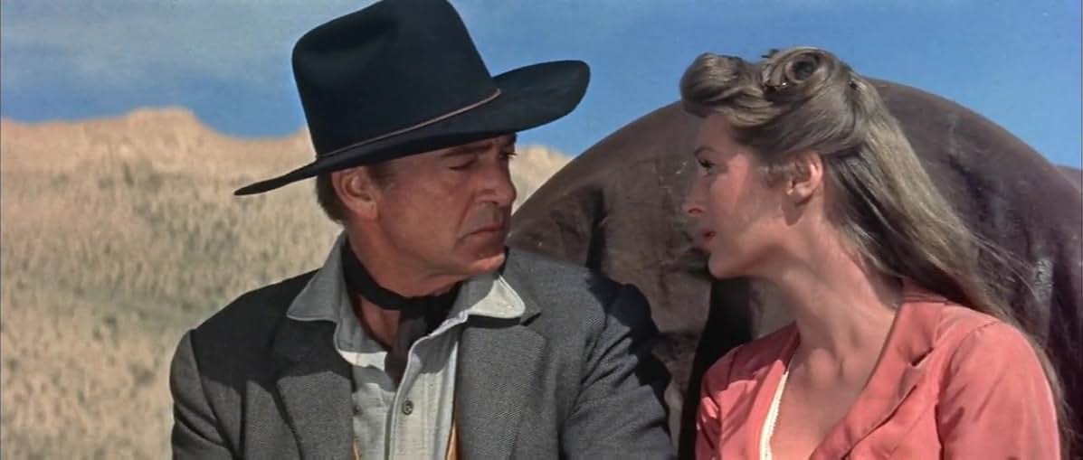 Gary Cooper and Billie London sit at the front of a covered wagon, looking into each other's eyes tenderly. A screenshot from Man of the West (1958).