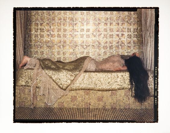 This may contain: a woman laying on top of a bed next to a wall covered in woven material