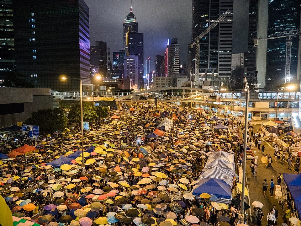 Street scene in Hong Kong. Crowds of protestors bearing umbrellas in urban streets.