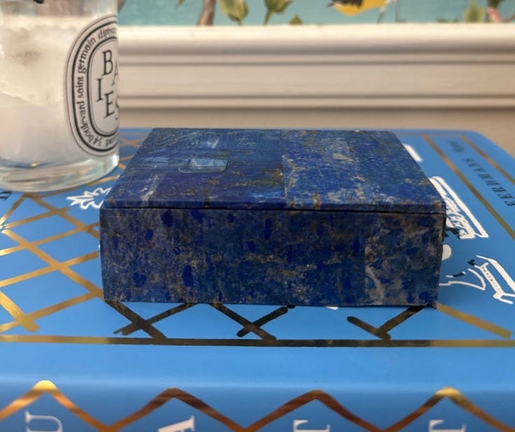 May include: A blue lapis lazuli box with gold flecks sitting on a blue book with gold trim. The book has the word 'ART' printed on the cover.