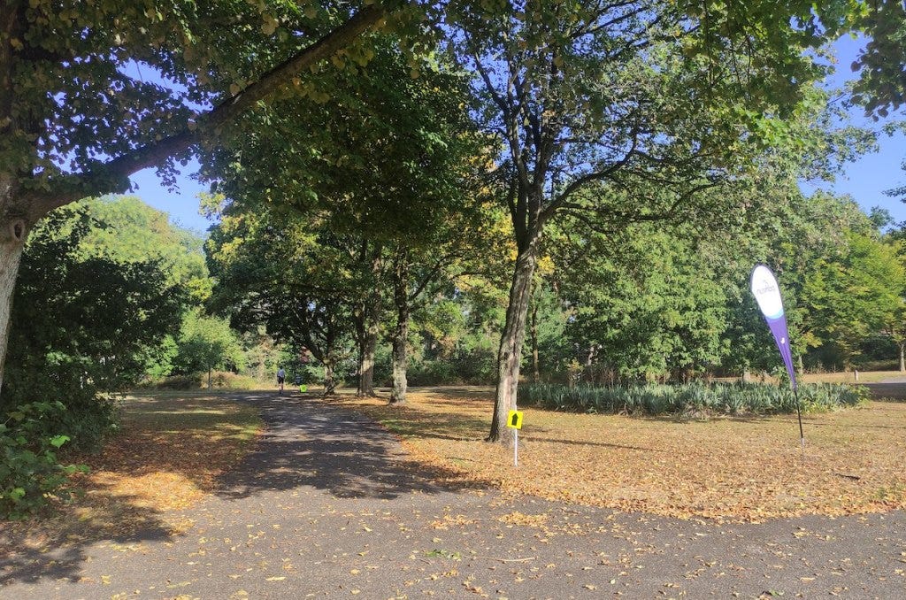An arrow points up the path to take people onto their second lap, under green-leafed trees.