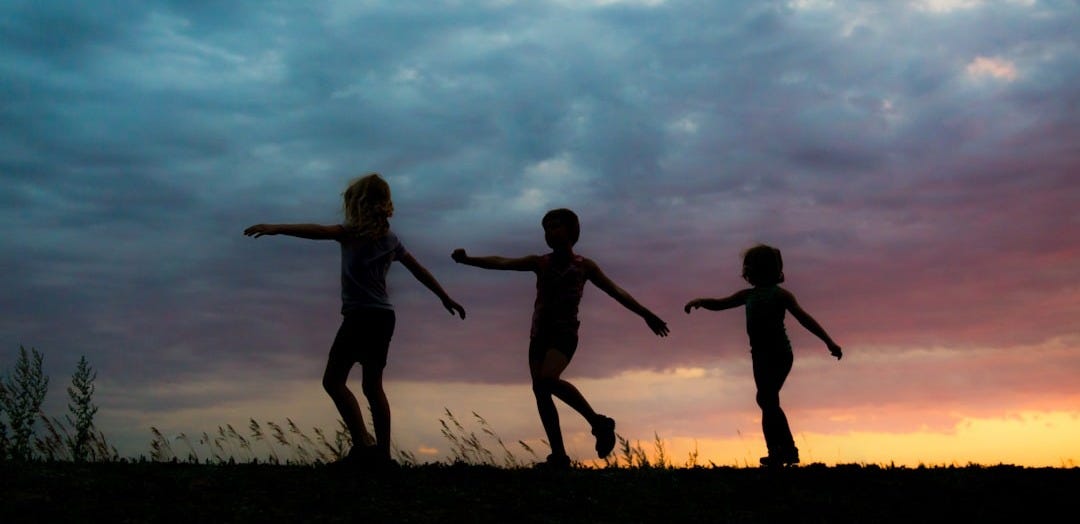 silhouette of 2 women jumping on grass field during sunset