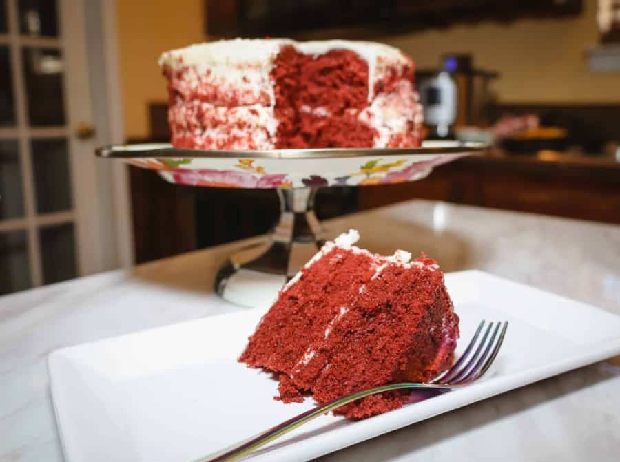 Slice of Southern red velvet cake with cream cheese frosting served beside a whole cake, a classic red dessert for Juneteenth celebrations and soul food holiday tables from The Soul Food Pot®