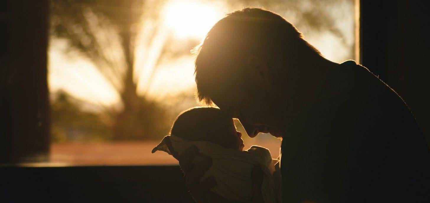 A father holding his baby in front of a glowing sunrise