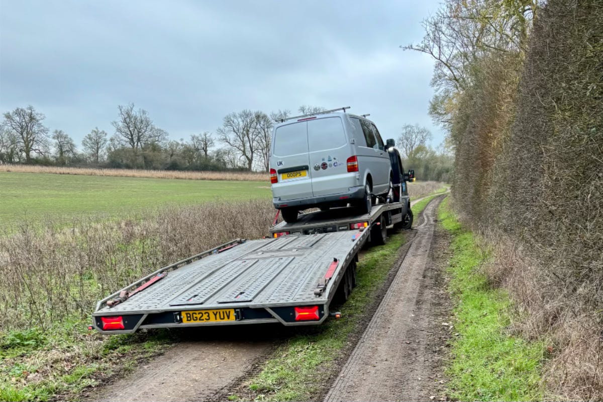 A van sits on a flatbed trailer in a muddy field. A van sits on a flatbed trailer in a muddy field.
