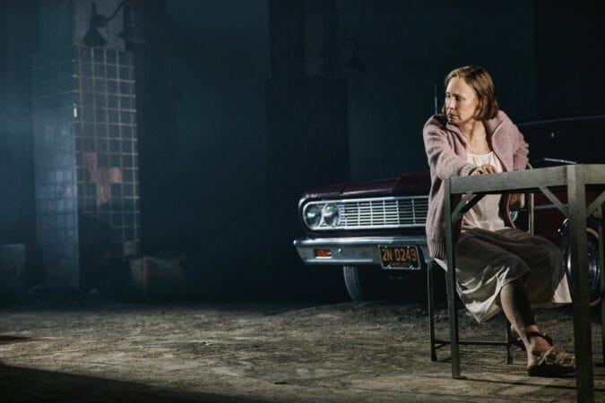 As Linda Loman, Laurie Metcalf sits at a table wearing a nightgown, looking distraught in a nondescript industrial space As Linda Loman, Laurie Metcalf sits at a table wearing a nightgown, looking distraught in a nondescript industrial space
