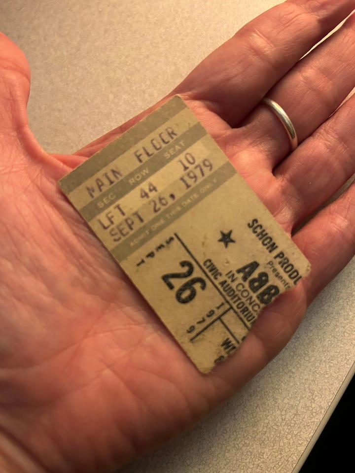 Left photo: a white man in drag is on the left, and a white man with a mustache is on the right. They stand in front of a wooden door, smiling. Right photo: a ticket stub from a 1979 ABBA concert rests in a white-skinned hand.