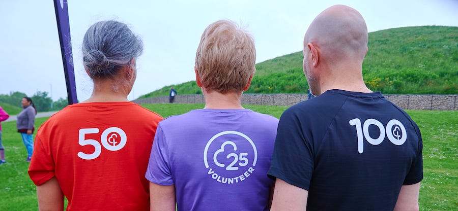 Three people wearing milestone Parkrun shirts with numbers 25, 50, and 100