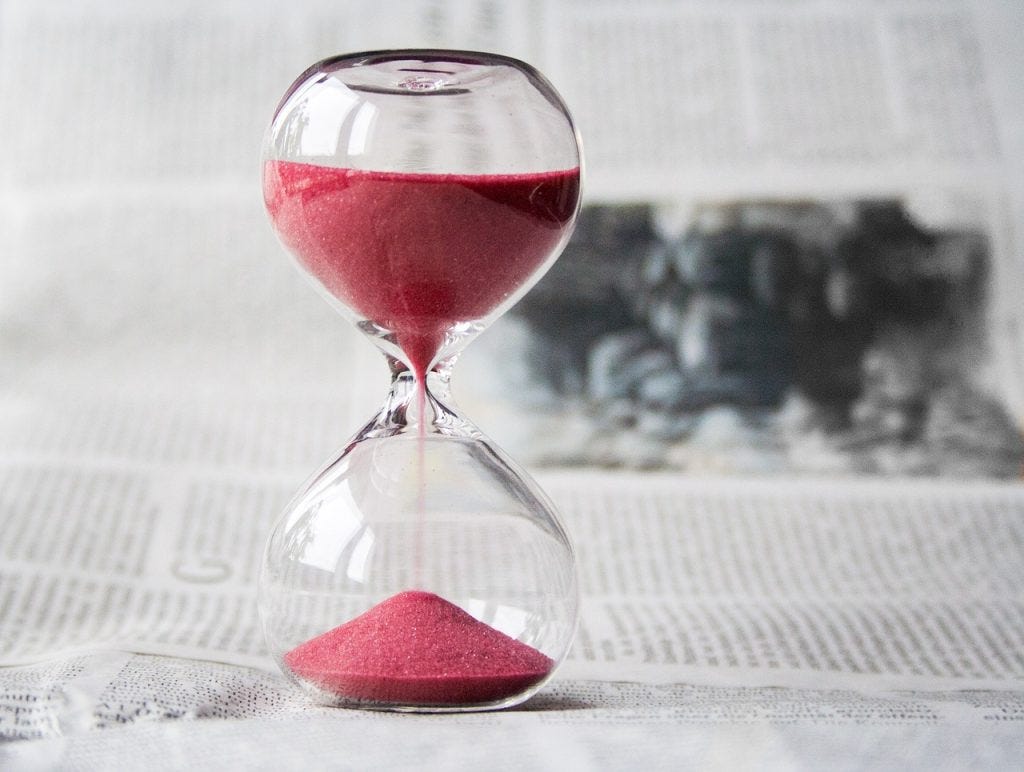 a clear hourglass with red fine sand flowing from the top to the bottom and landing on a growing pyramid of red sand in the bottom a clear hourglass with red fine sand flowing from the top to the bottom and landing on a growing pyramid of red sand in the bottom