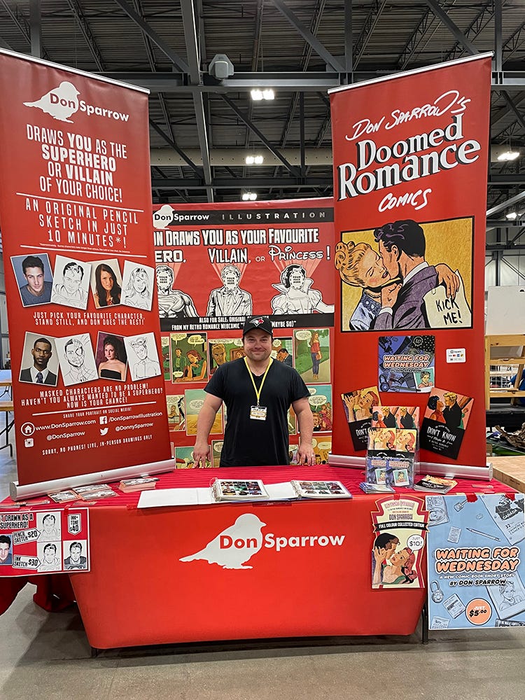Revered Canadian cartoonist Don Sparrow standing at his table display at Regina Expo 2023.  The towering display is red and white, with retro comics throughout.