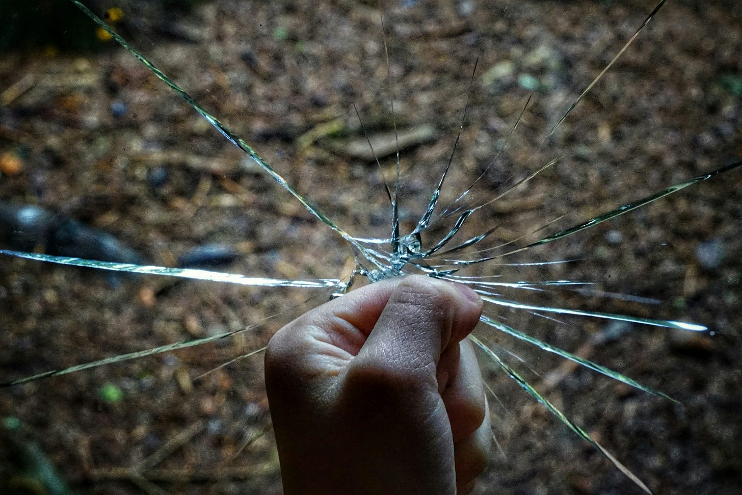A clenched fist striking shattered glass, cracks radiating outward from the point of impact.
