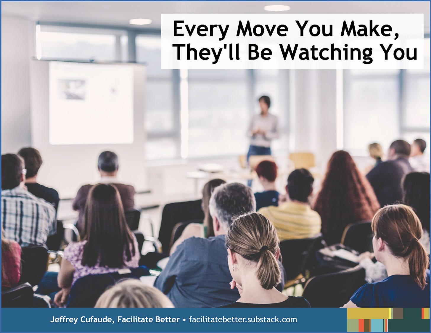 view from behind approximately 20 people seated in rows watching a presentation at a conference