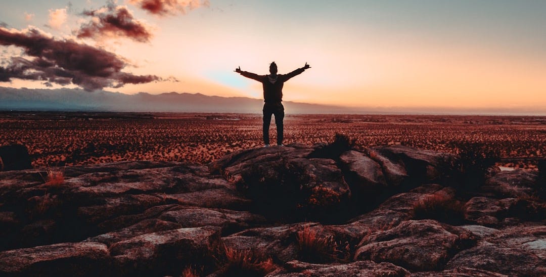 person standing on rock raising both hands