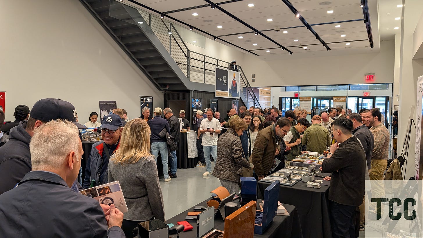 Crowded indoor scene near the entrance of Windup Watch Fair. People gather around watch and accessory booths while others queue near tables. The space is modern and brightly lit, with signage for TypSIM and Rapport visible.