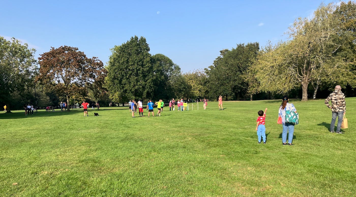 A small child points at the sky while runners behind finish in a funnel marked by tape