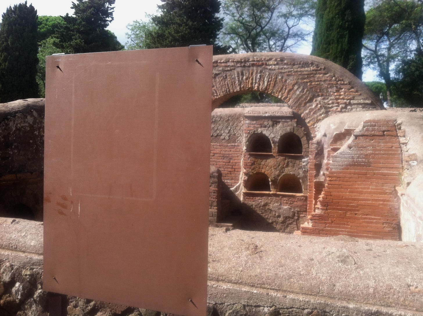a color photo of a blank sign or placard that's in front of some kind of historical Roman ruins