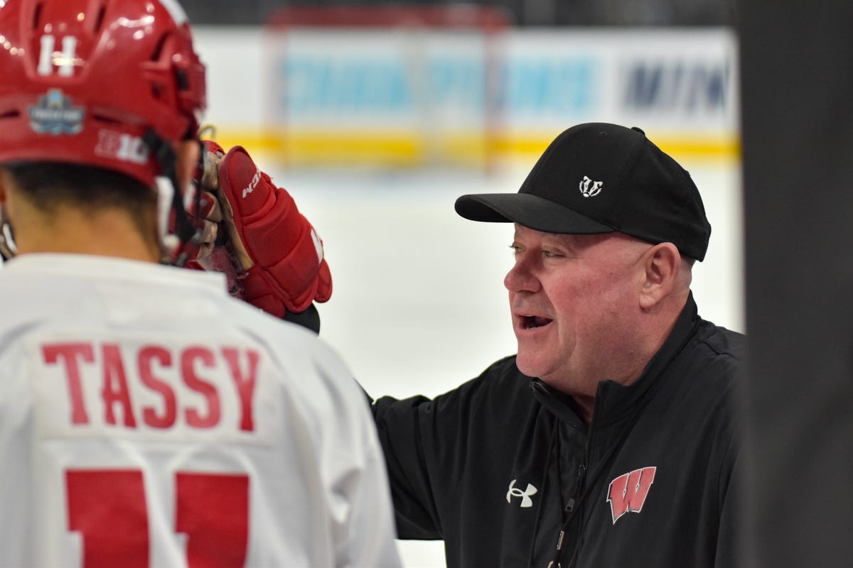 Mike Hastings, Wisconsin hockey coach, in a black jacket and black hat speaks with Simon Tassy Mike Hastings, Wisconsin hockey coach, in a black jacket and black hat speaks with Simon Tassy