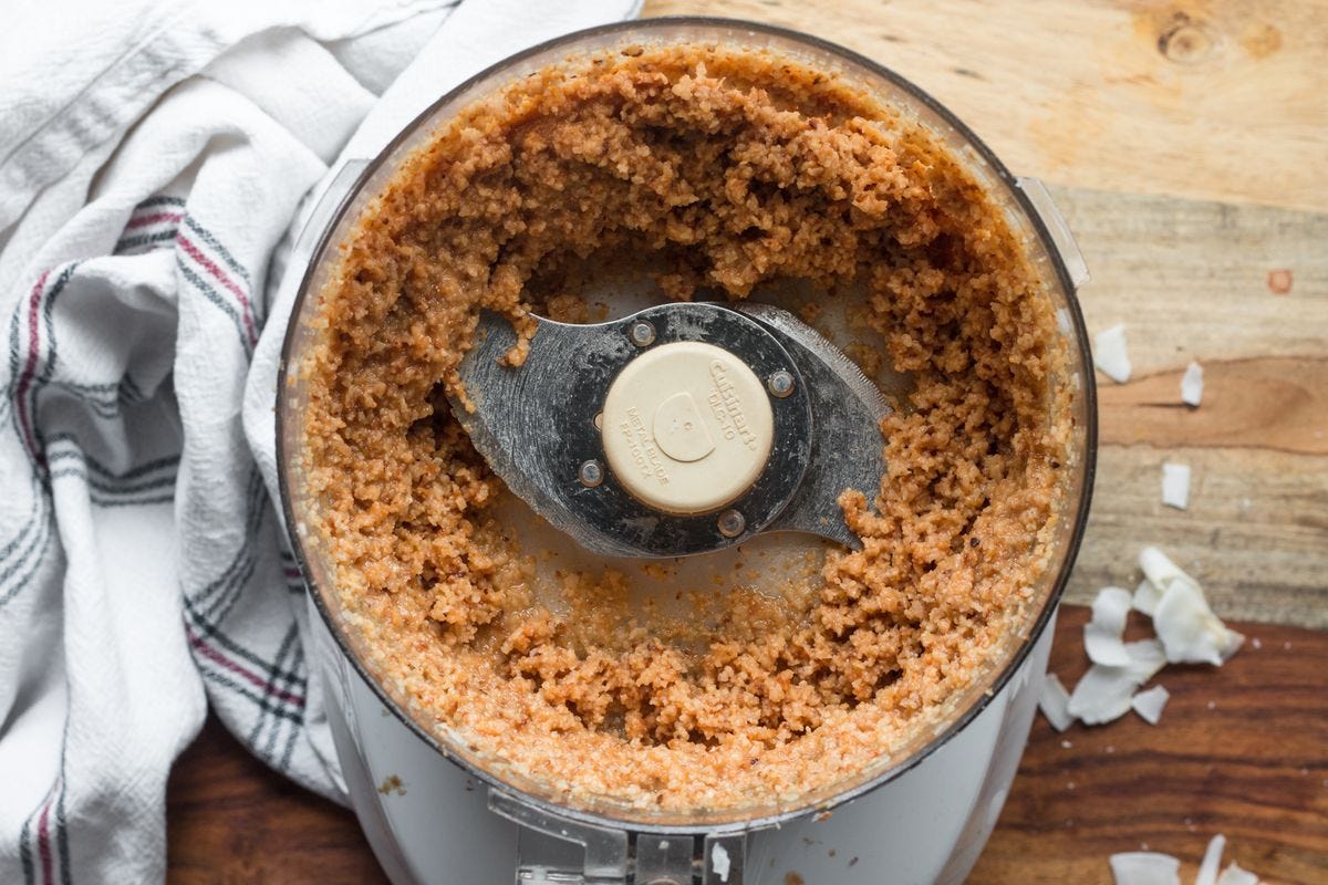 Overhead shot of food processor with finely ground coconut. White kitchen towel. Overhead shot of food processor with finely ground coconut. White kitchen towel.