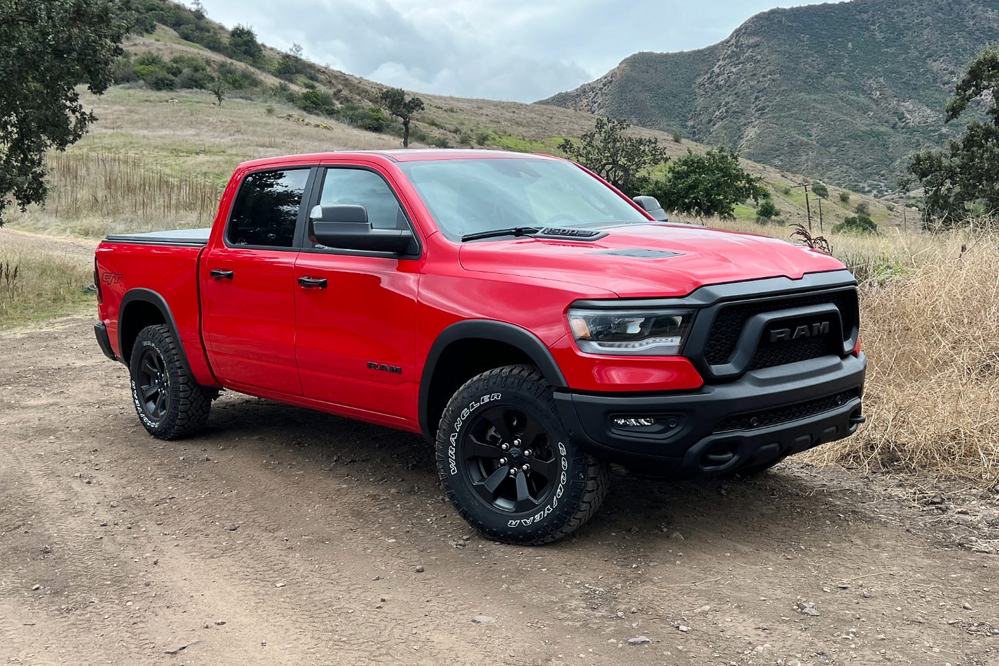 A red Ram 1500 Rebel is parked on a mountain trail on a cloudy day in California