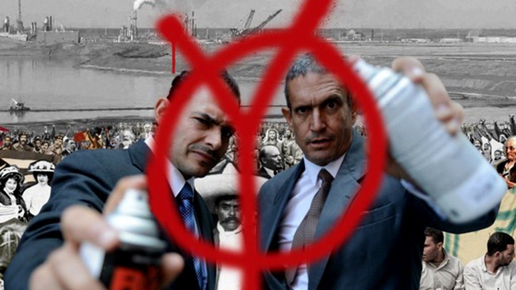 Two men spray paint a "Y" version of the anarchist circled "A" with spray paint.