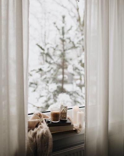 This may contain: a window sill with candles and a cup on it in front of a snowy tree