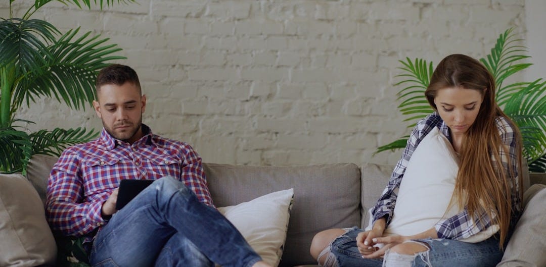 Couple sitting on sofa looking at phones