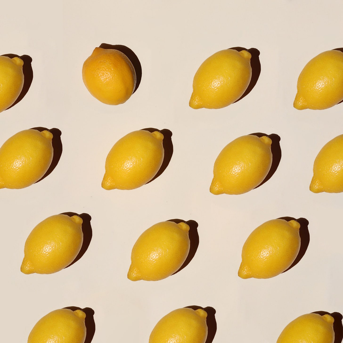 several lemons are lined diagonally on an off white table. several lemons are lined diagonally on an off white table.