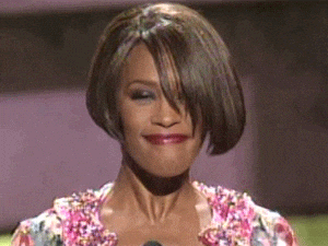 GIF of Whitney Houston smiling with a tight-lipped, knowing expression and slightly raised eyebrows