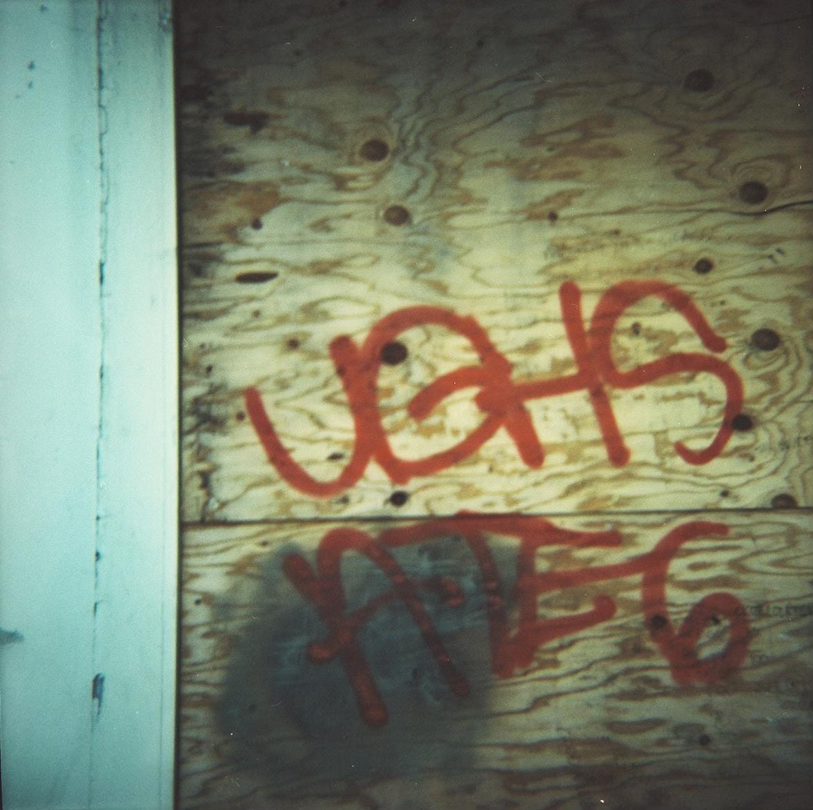 A blurry film photograph of indecipherable red letters tagged on a piece of plywood.