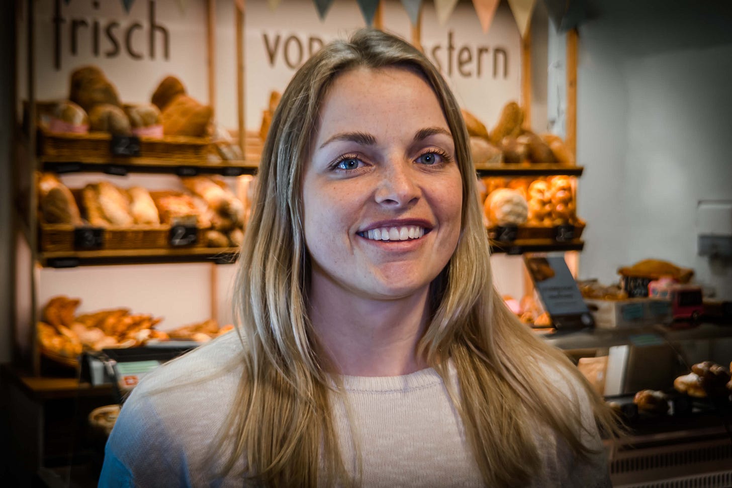 Michaela Schöni steht lächelnd in der „äss-bar“ in Bern, einem Laden, der Brot und Backwaren vom Vortag verkauft. Hinter ihr sind Regale mit Broten und Zöpfen zu sehen, darüber die Aufschrift „frisch vom Vortag“. Michaela Schöni steht lächelnd in der „äss-bar“ in Bern, einem Laden, der Brot und Backwaren vom Vortag verkauft. Hinter ihr sind Regale mit Broten und Zöpfen zu sehen, darüber die Aufschrift „frisch vom Vortag“.