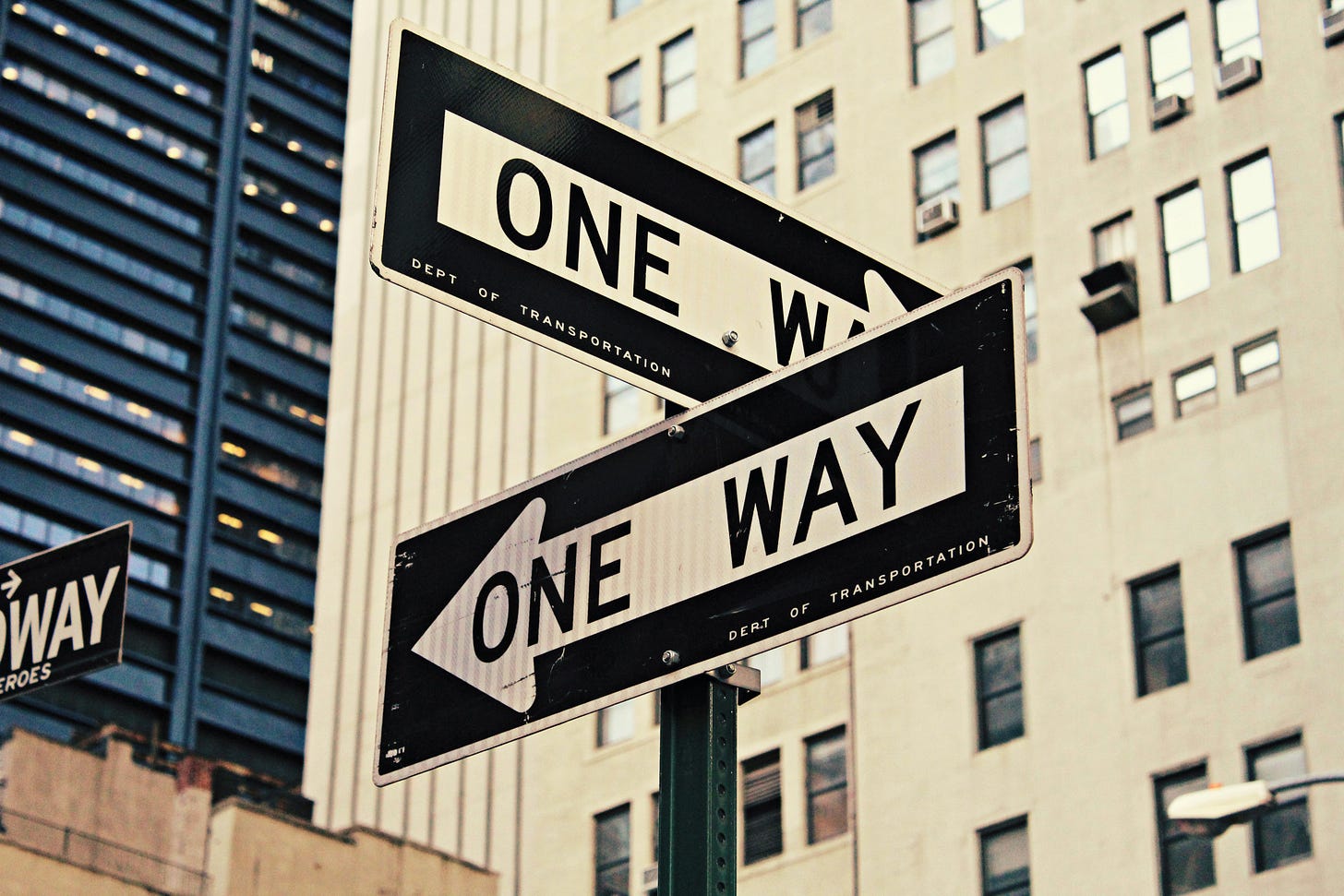Crossing one way street signs with skyscrapers in the background.