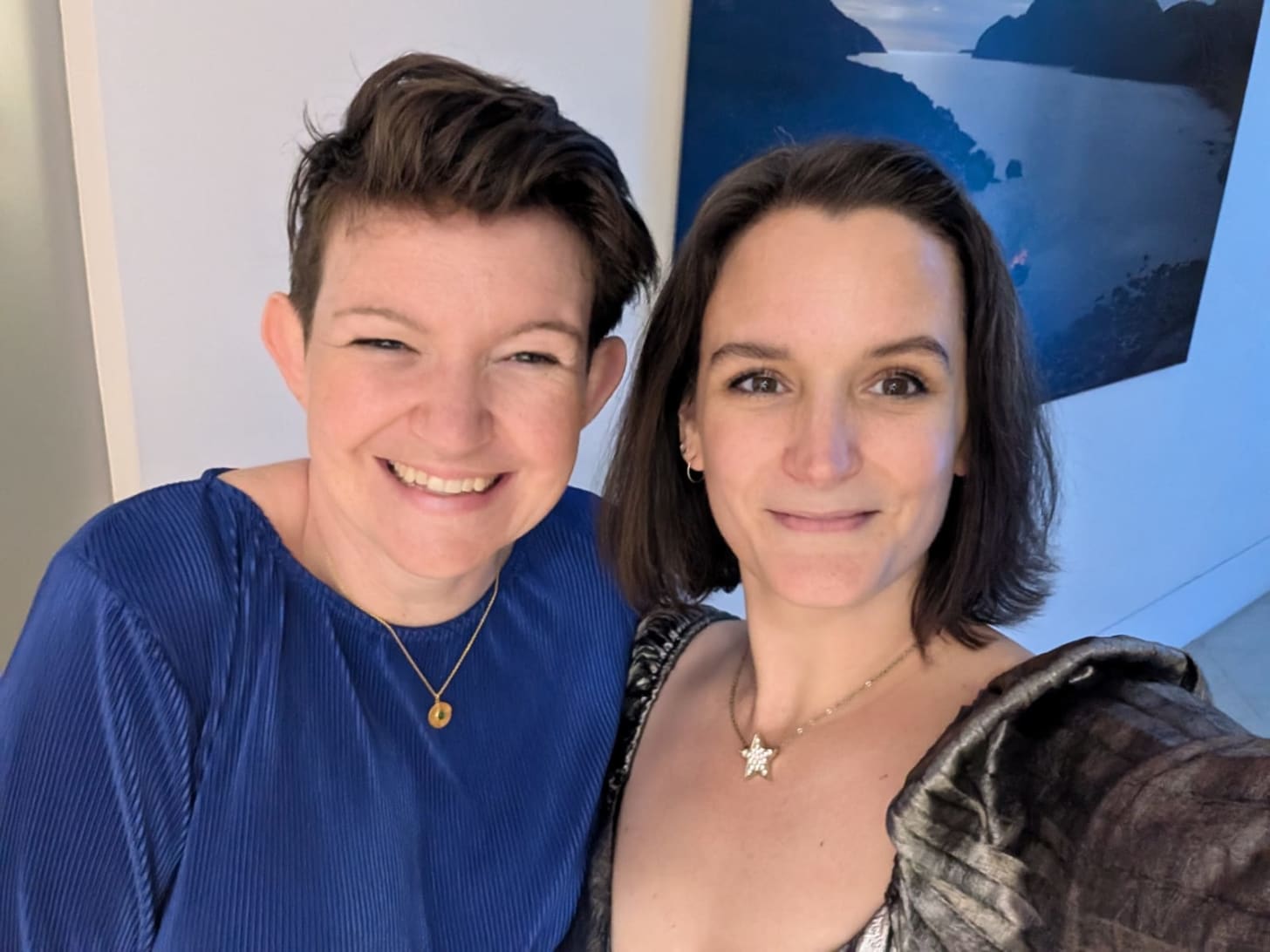 Molly Scanlan has cool short brown hair, Mel has a short bob of brown hair, both are white women smiling with their eyes but not their teeth. Molly has a royal blue top, Mel has a shimmery metallic dress. 
