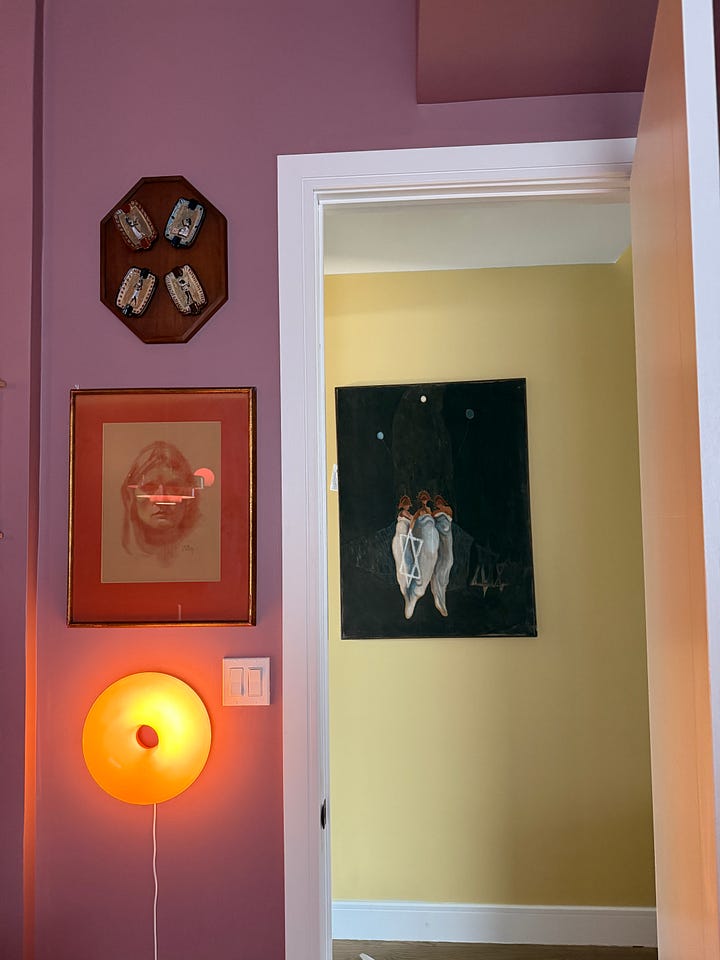 Two images from Melissa Geurts' home showing items from Susanne Hilberry's estate: left image shows a handmade ceramic pot with yellow and brown glazing on a red surface; right image shows a colorful wall with framed artwork including an illuminated orange circular piece and various gallery prints