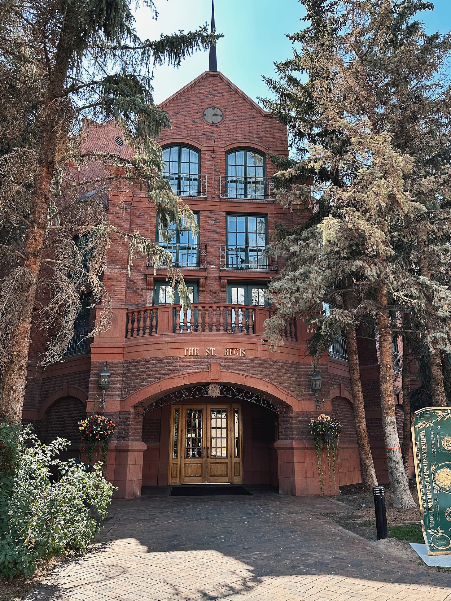 Red-brick exterior and arched entrance of the St. Regis Aspen Resort, framed by tall evergreen trees.