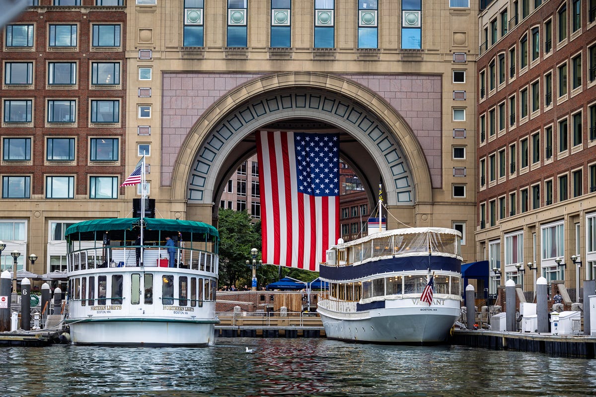 Boats docked at Rowes Wharf with large American flag hanging from the archway in Boston Harbor