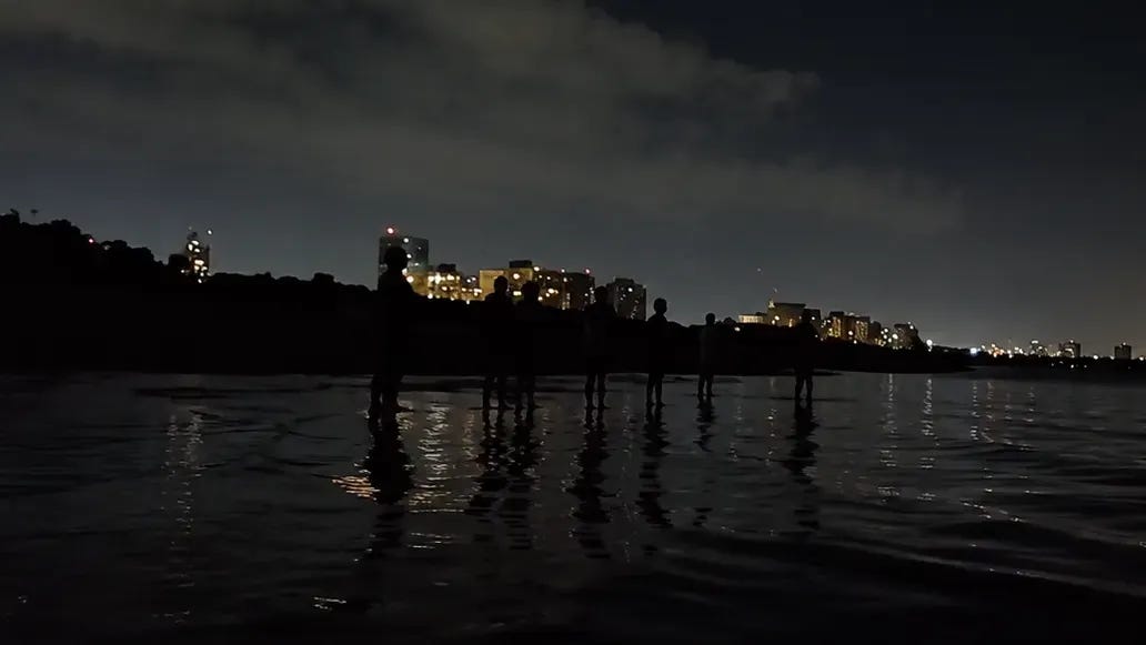A group of people standing like zombies in the water after dark, looking into the distance