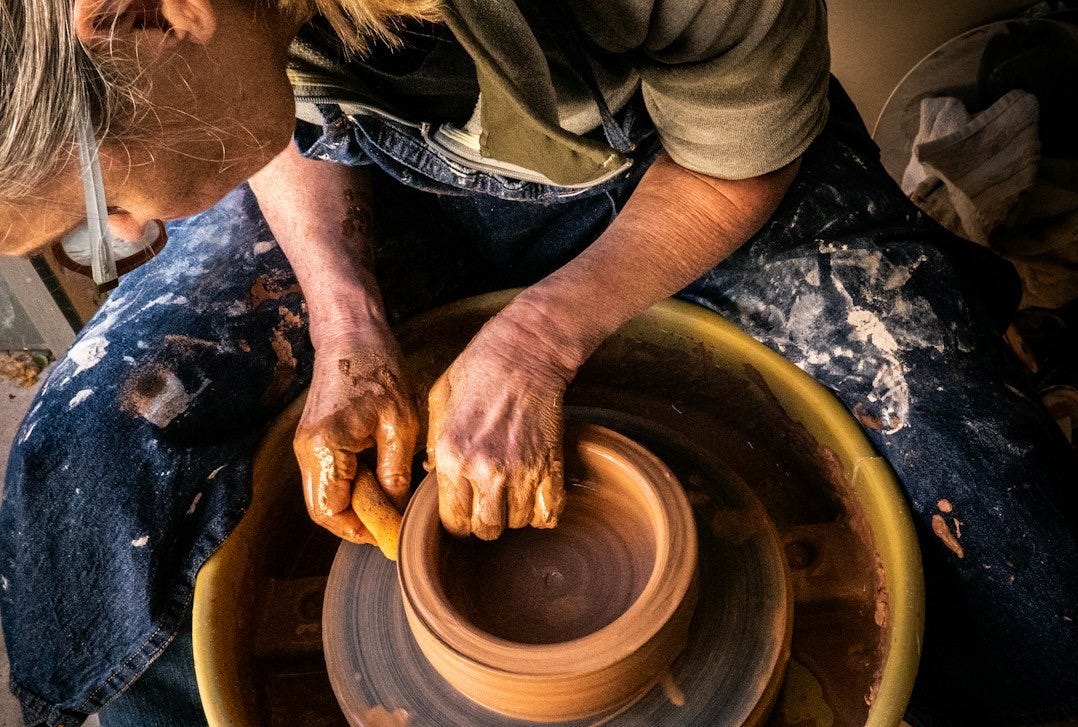person in blue denim jeans making clay pot