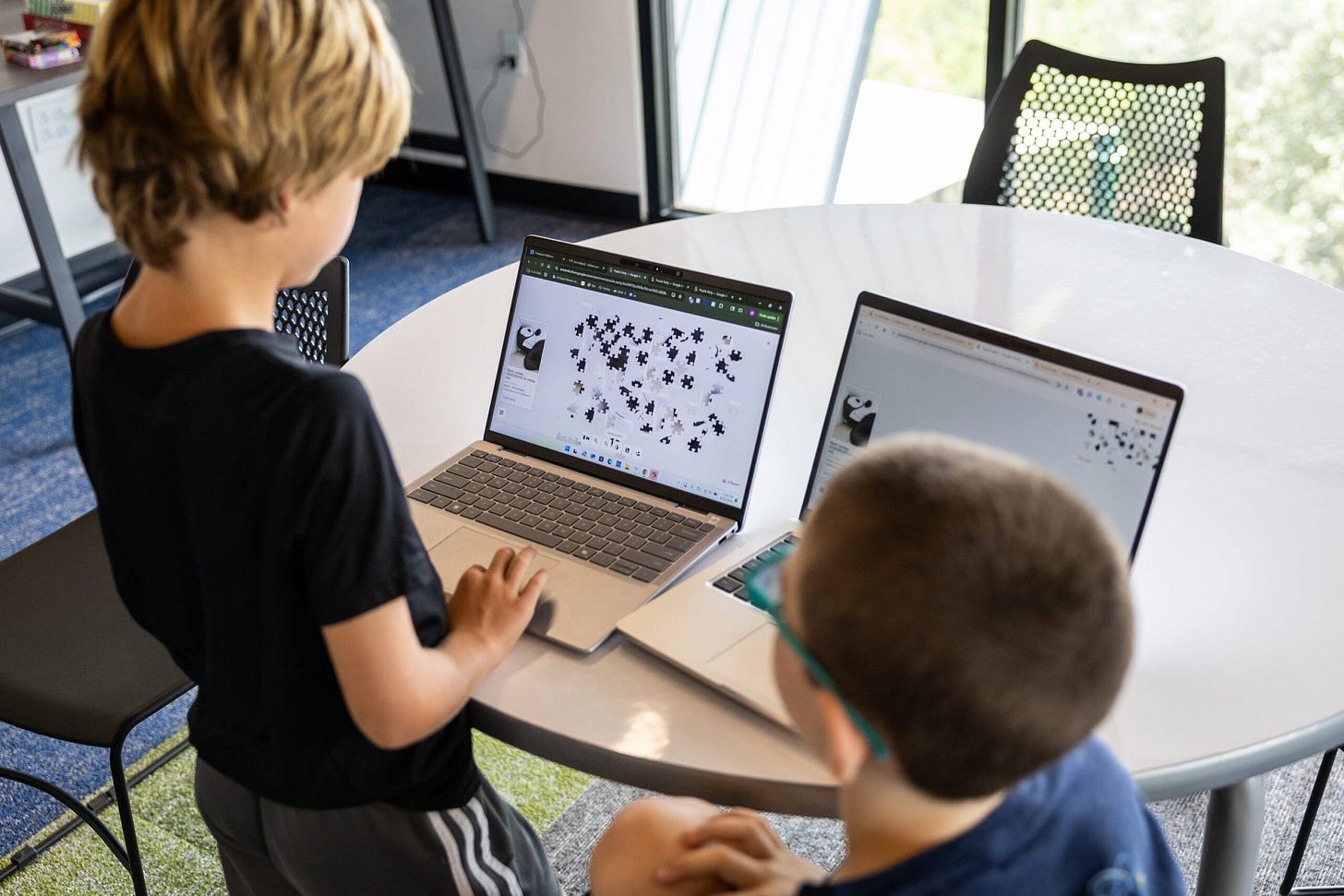 Two young kids solve a digital jigsaw puzzle on laptops