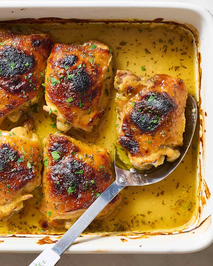 Baked chicken thighs in a white dish, golden brown with crispy skin, surrounded by flavorful juices.