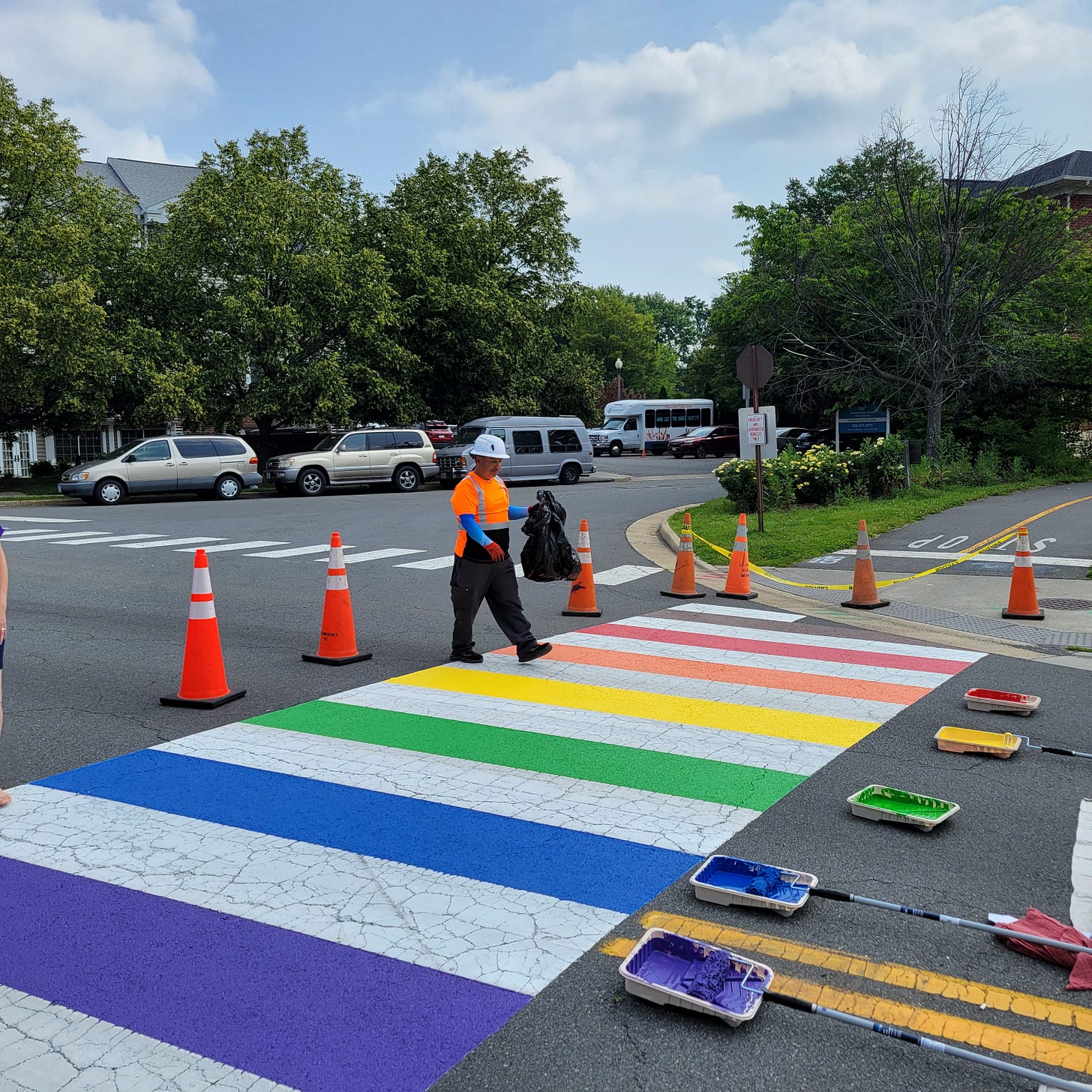 A man painting a vibrant rainbow crosswalk on a city street, showcasing colorful stripes on the pavement.