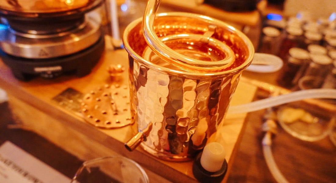 A cooper distilling container with a copper tube in it, on top of a wooden board A cooper distilling container with a copper tube in it, on top of a wooden board