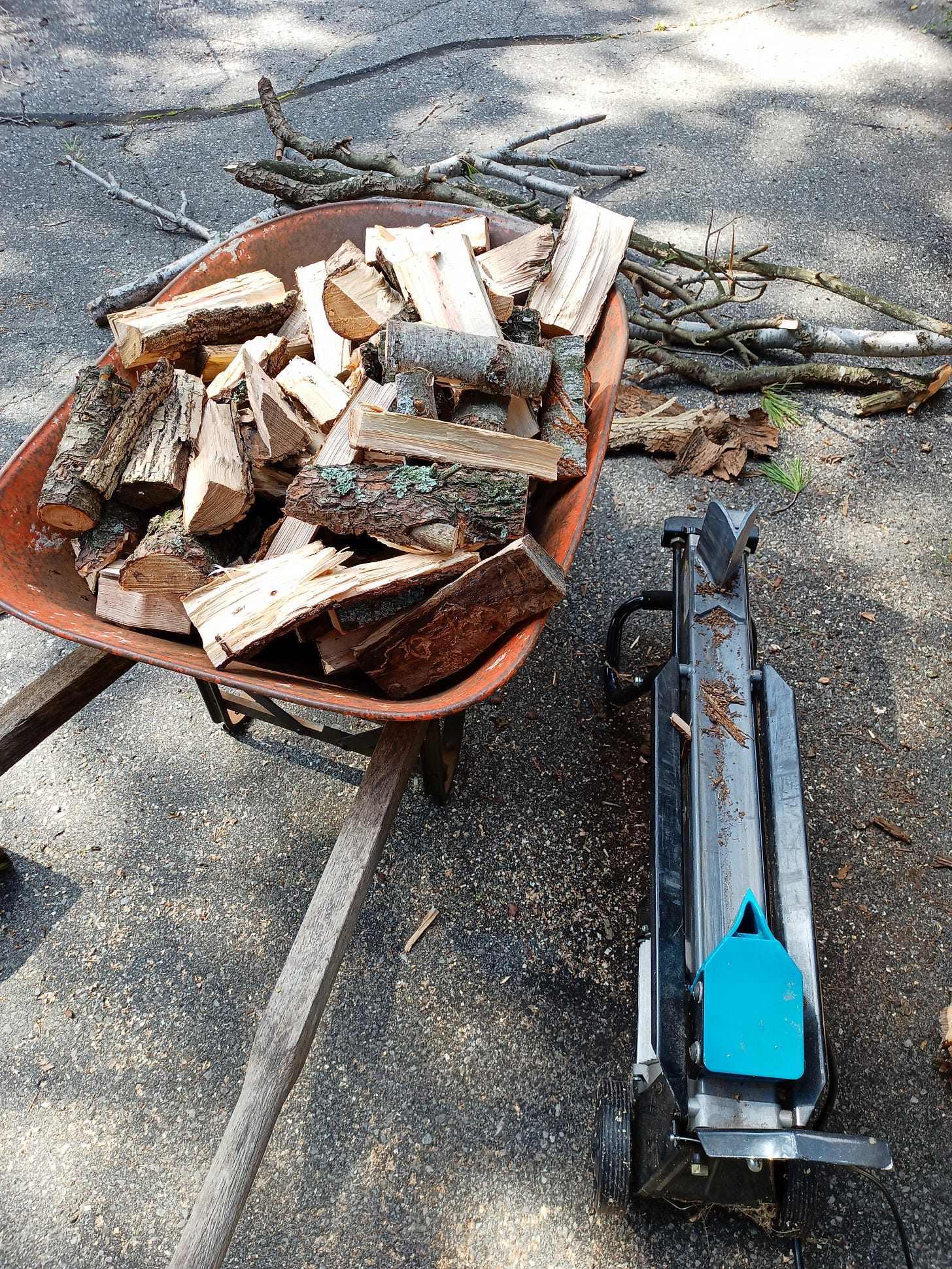 A wheelbarrow full of kindling-sized wood, beside an electric log splitter.