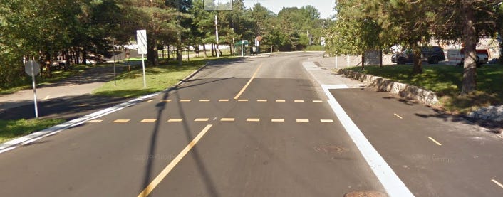 A two lane road with a trail on the right side, and switching to the left side across a well marked crossing.