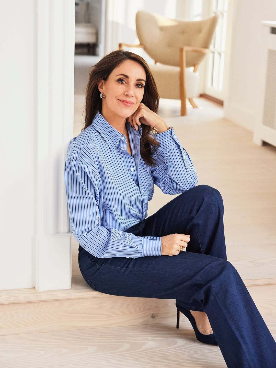 Woman in stripy blue shirt and blue trousers smiling for the camera while seated in a doorway